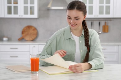 Photo of Beautiful young woman with notebook at white marble table in kitchen