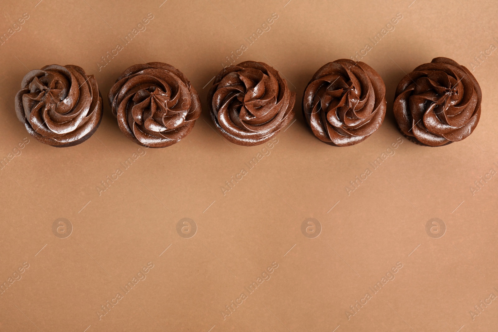 Photo of Delicious chocolate cupcakes with cream on brown background, flat lay. Space for text