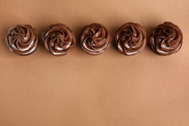 Delicious chocolate cupcakes with cream on brown background, flat lay. Space for text