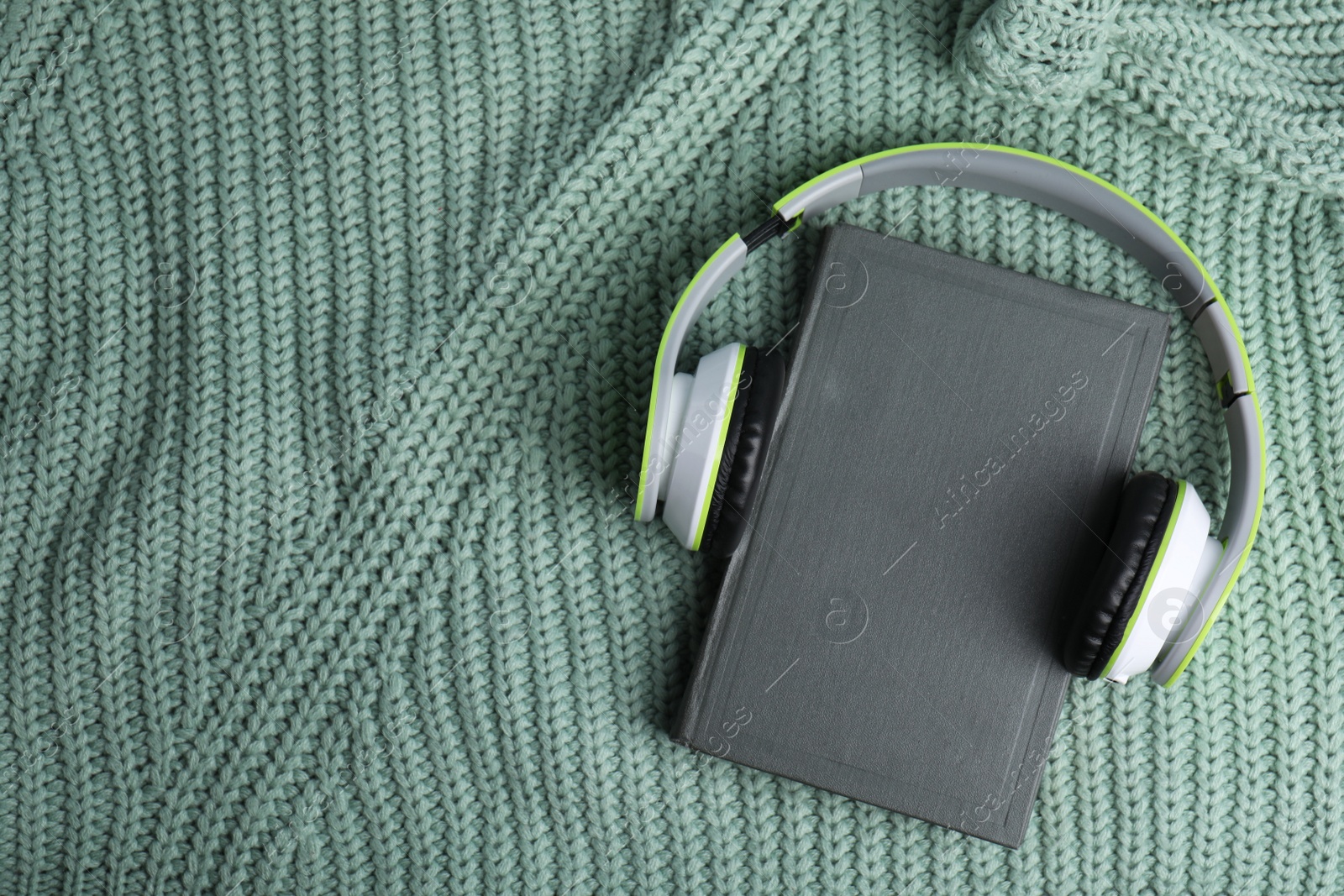 Photo of Modern headphones with hardcover book on knitted sweater, top view