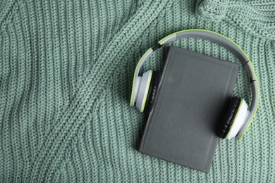 Photo of Modern headphones with hardcover book on knitted sweater, top view