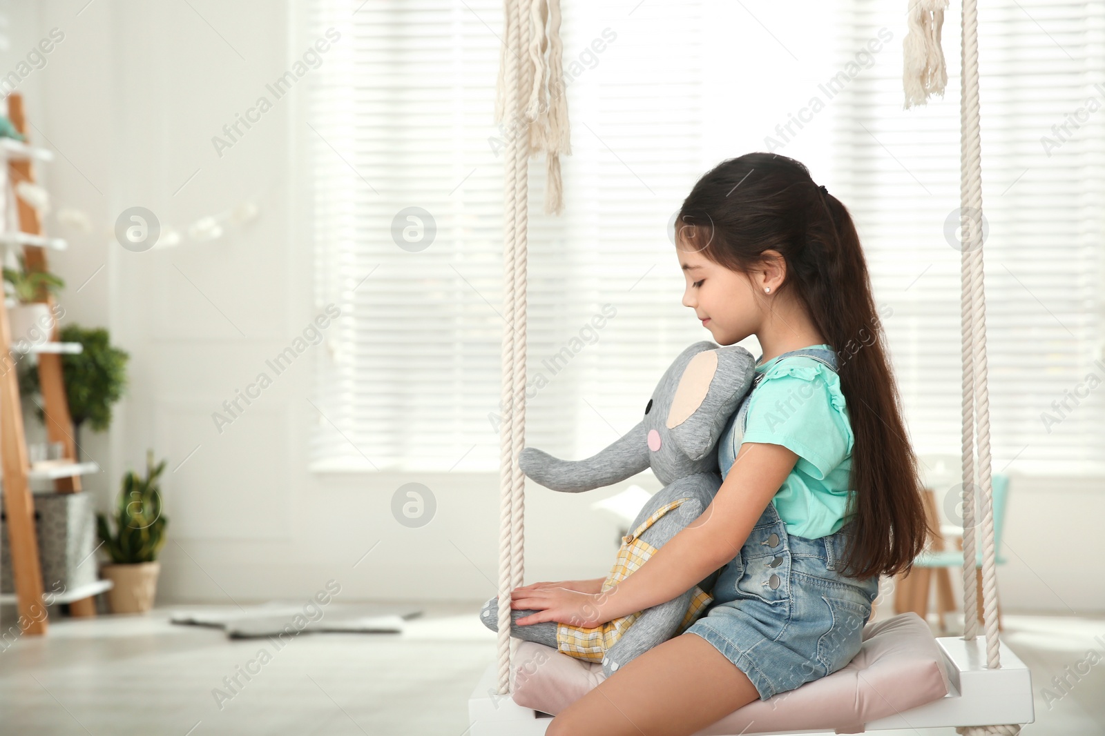 Photo of Cute little girl playing with toy elephant on swing at home. Space for text