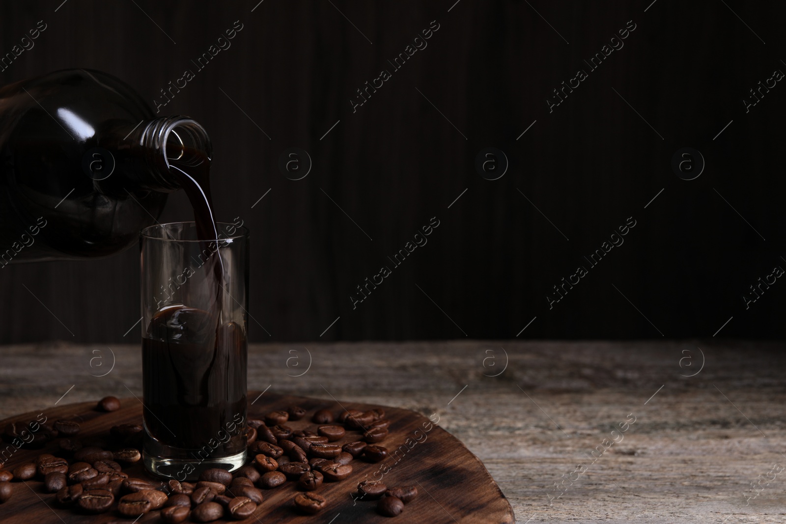 Photo of Pouring coffee liqueur into glass and beans on wooden table, space for text