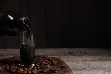 Photo of Pouring coffee liqueur into glass and beans on wooden table, space for text