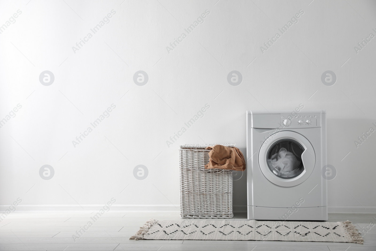 Photo of Modern washing machine and laundry basket near white wall indoors, space for text. Bathroom interior