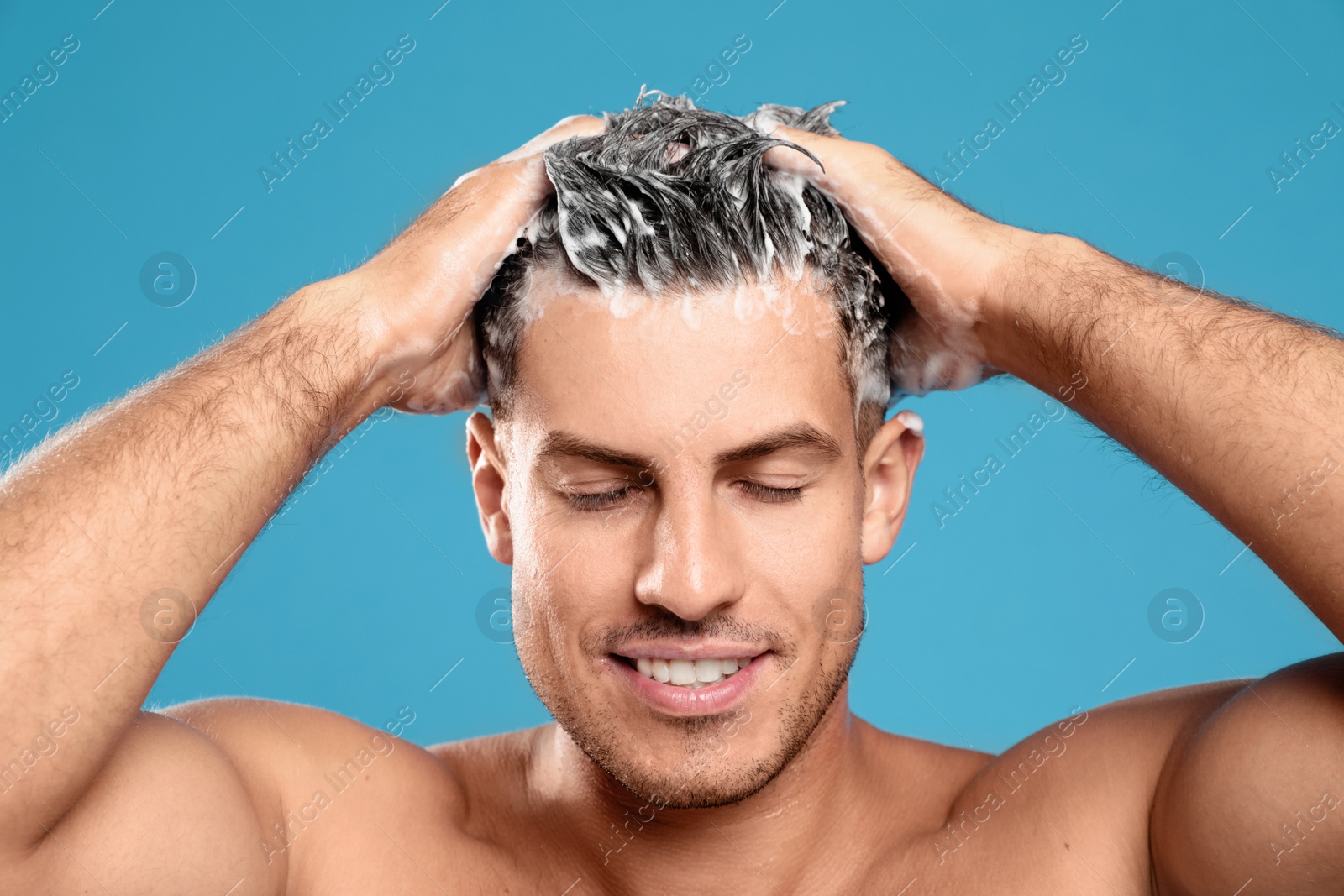 Photo of Handsome man washing hair on light blue background