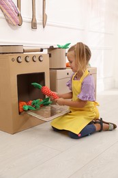 Photo of Little girl playing with toy cardboard oven at home