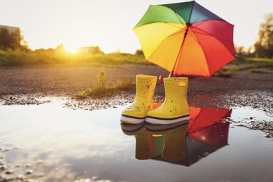 Photo of Yellow rubber boots and umbrella in puddle outdoors, space for text. Autumn walk