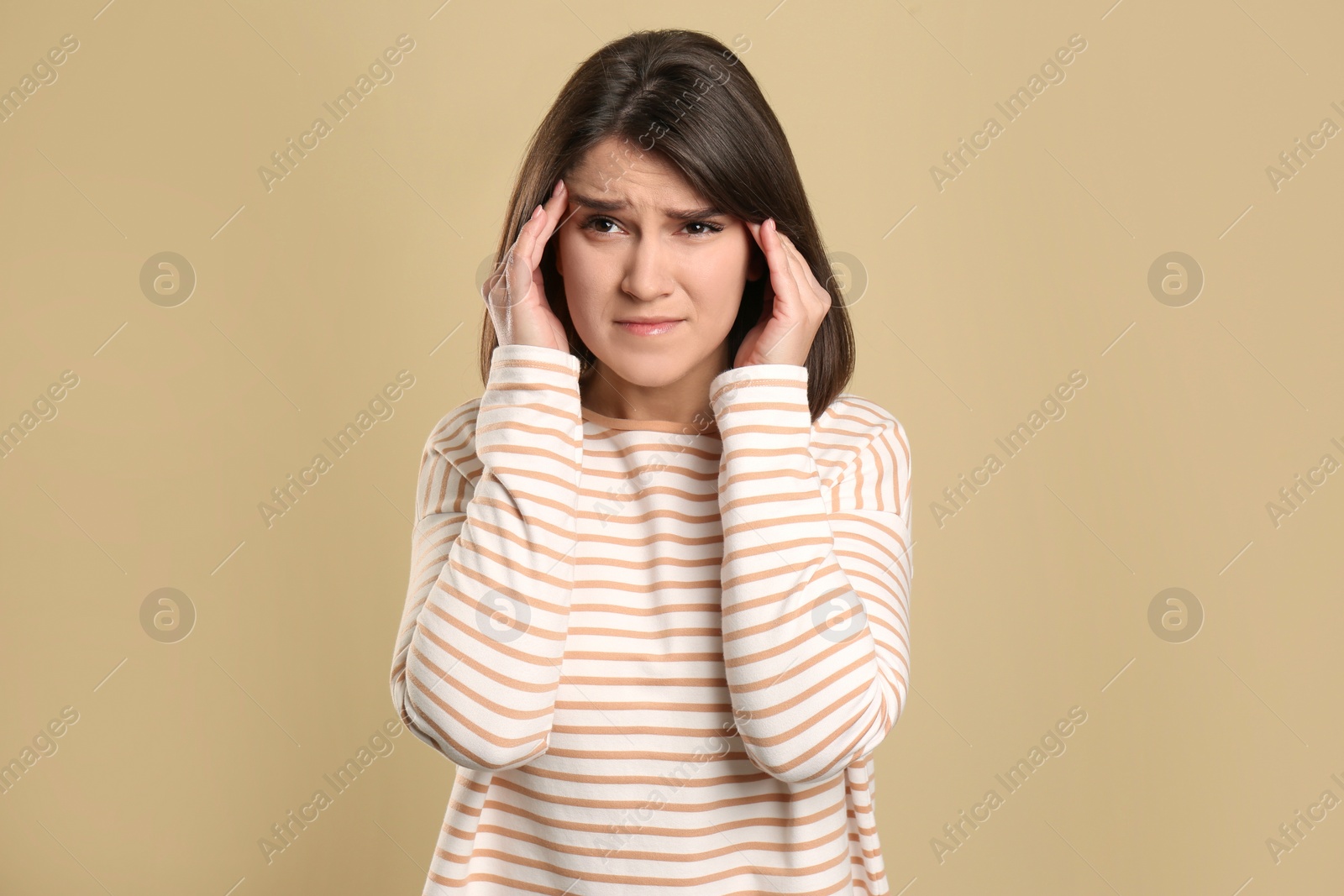 Photo of Young woman suffering from migraine on beige background