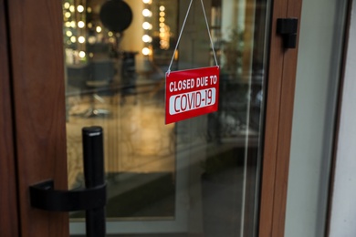 Photo of Red sign with words Closed Due To Covid-19 hanging on glass door