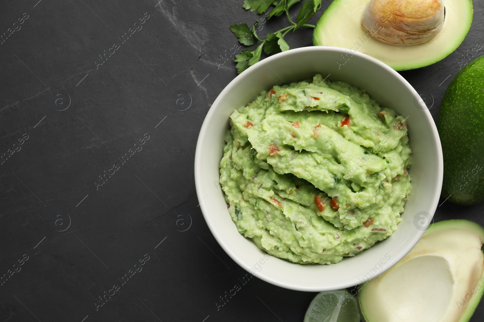 Photo of Delicious guacamole, fresh avocado and parsley on dark grey table, flat lay. Space for text