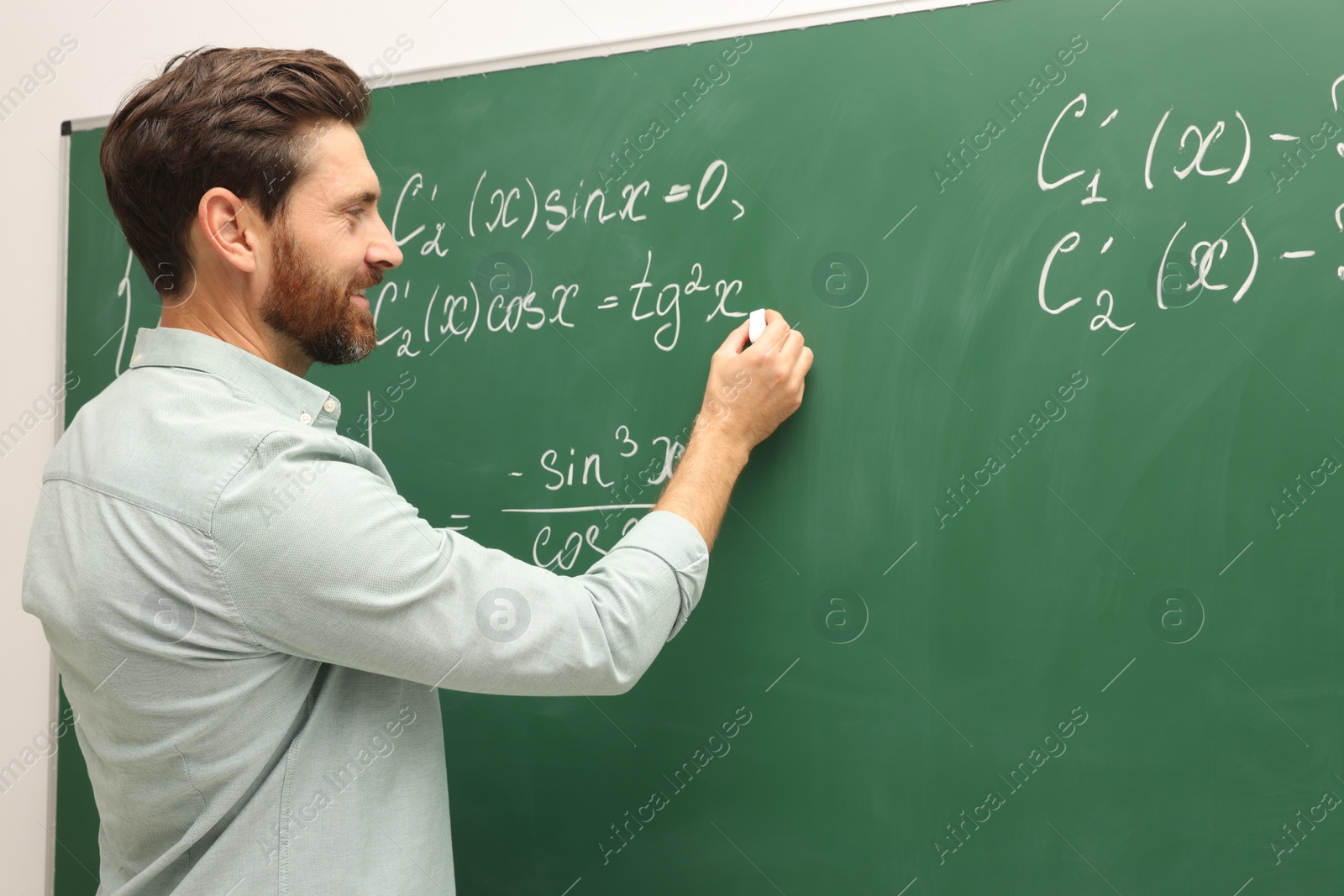 Photo of Happy teacher explaining mathematics at chalkboard in classroom