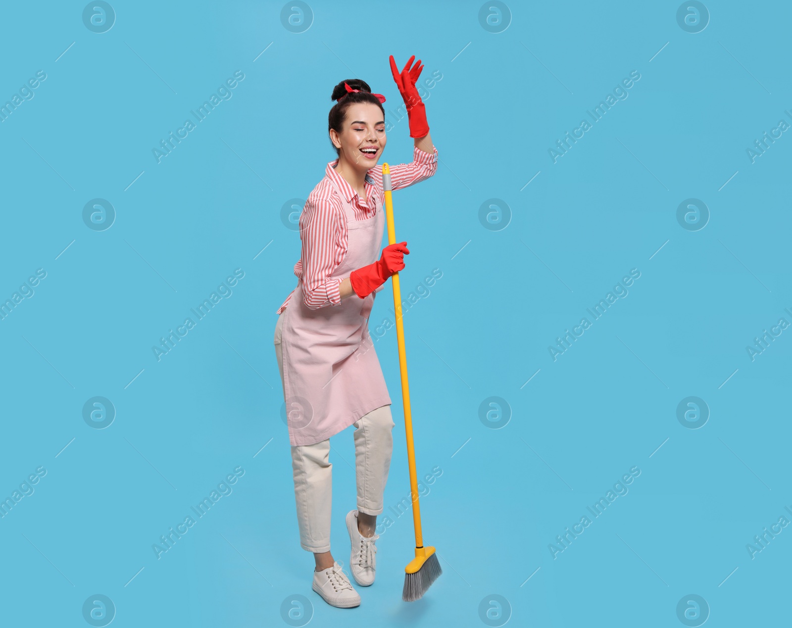 Photo of Young housewife with broom having fun on light blue background