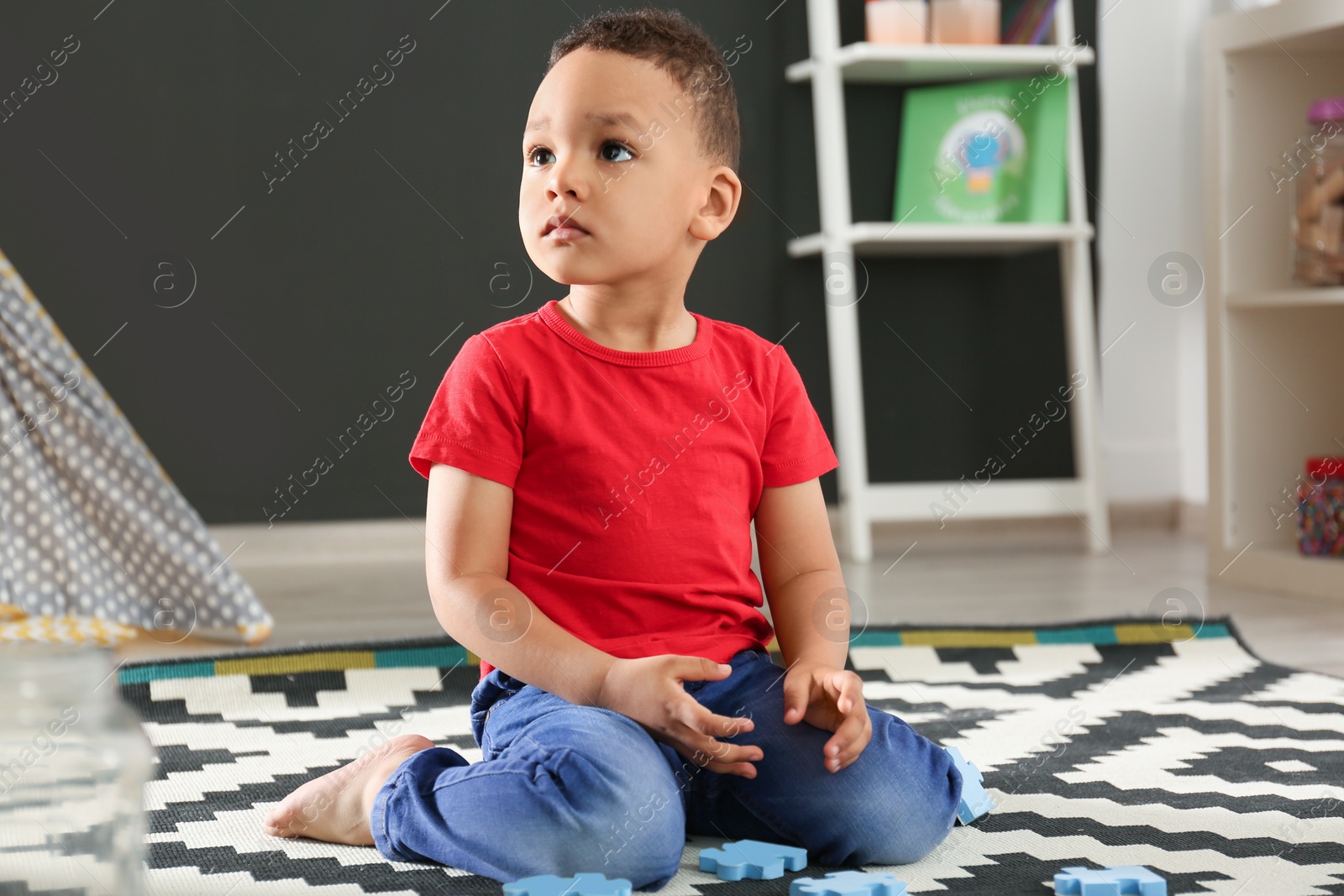 Photo of Cute little African-American child playing with puzzles on floor in kindergarten. Indoor activity