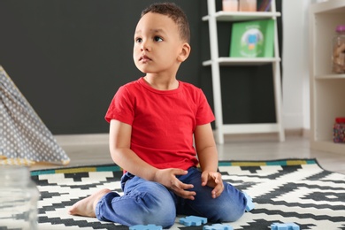 Cute little African-American child playing with puzzles on floor in kindergarten. Indoor activity