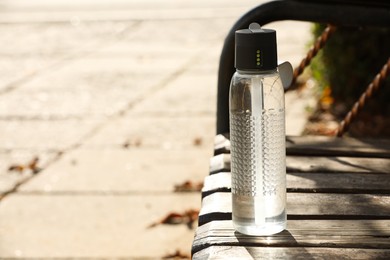 Photo of Sport bottle of water on wooden bench outdoors, space for text