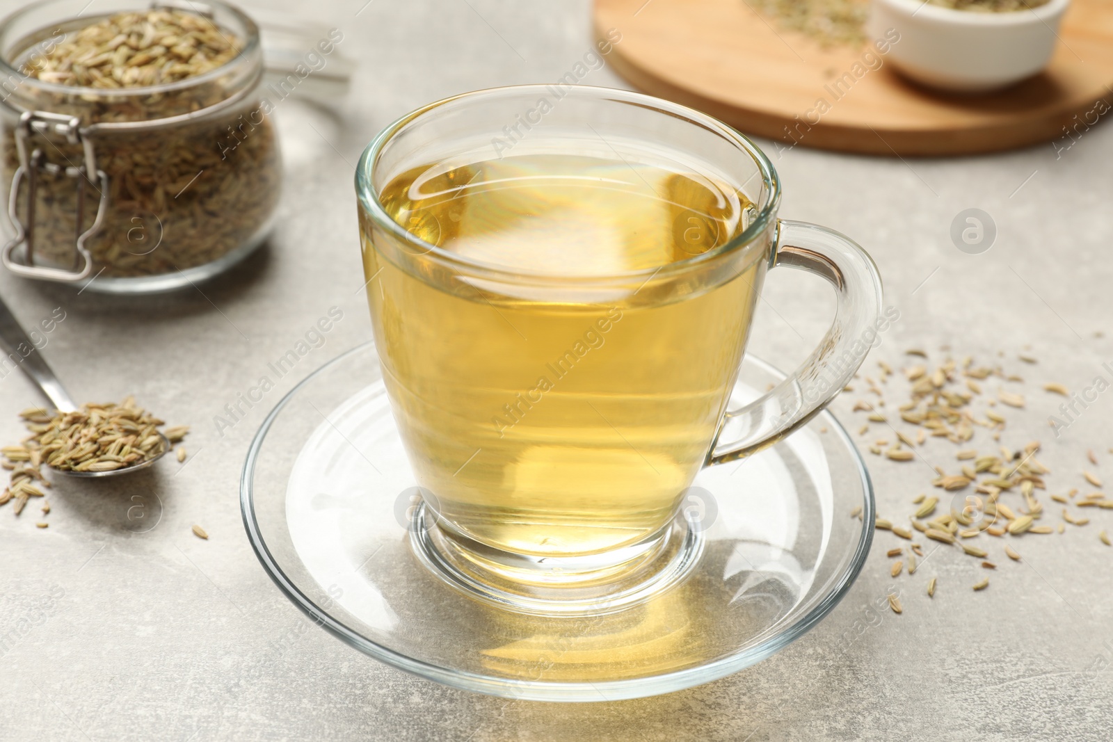 Photo of Aromatic fennel tea and seeds on light grey table, closeup