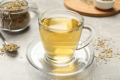 Photo of Aromatic fennel tea and seeds on light grey table, closeup