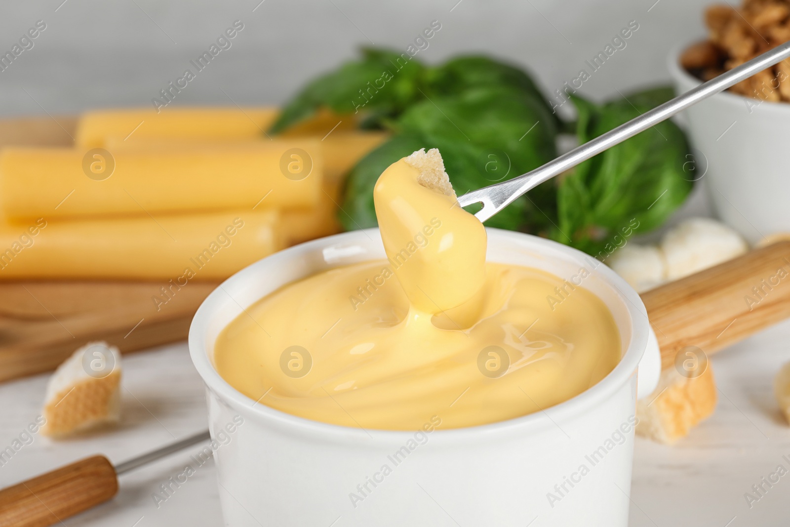 Photo of Pot of tasty cheese fondue and products on white wooden table, closeup view