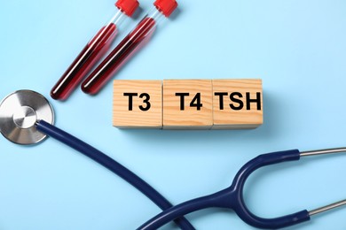 Photo of Endocrinology. Stethoscope, wooden cubes with thyroid hormones and blood samples in test tubes on light blue background, flat lay