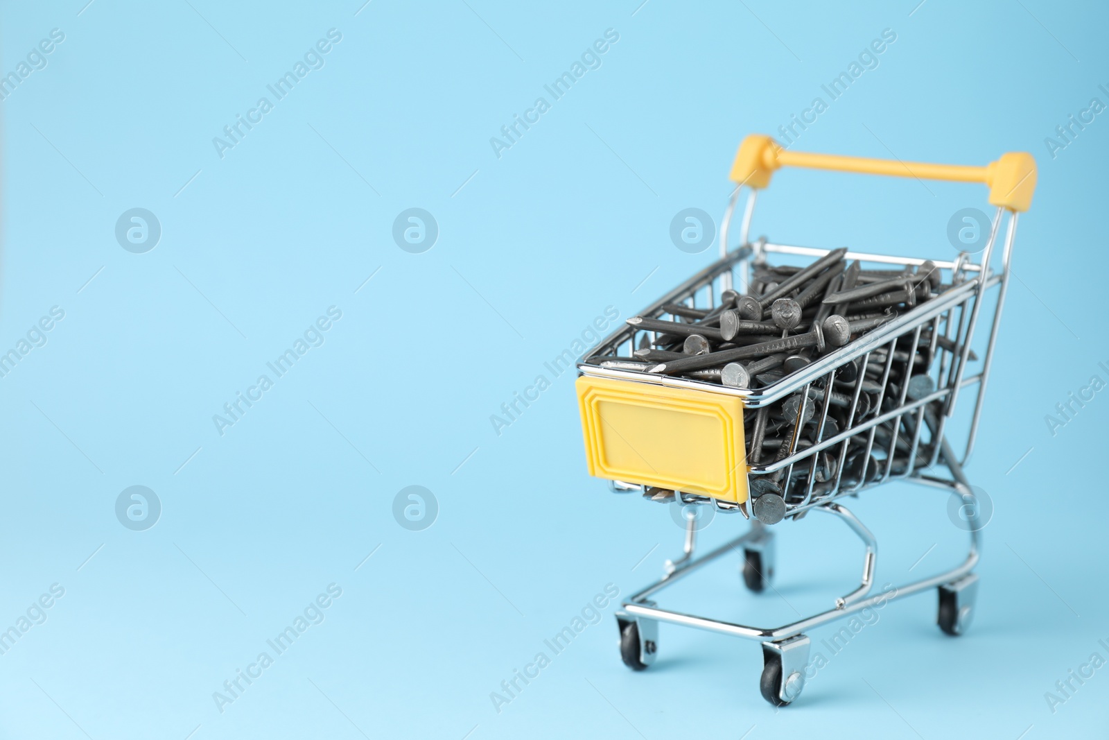 Photo of Metal nails in shopping cart on light blue background, space for text