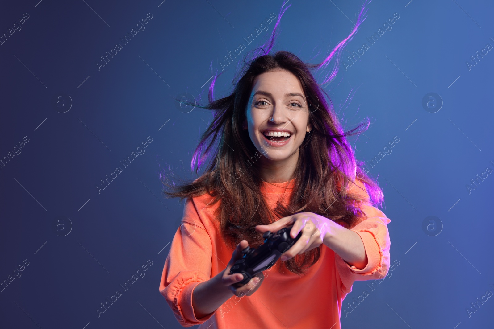 Photo of Emotional woman playing video game with controller on dark blue background