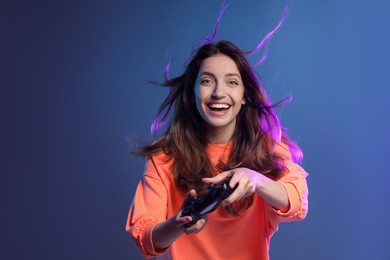 Photo of Emotional woman playing video game with controller on dark blue background