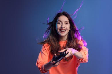 Emotional woman playing video game with controller on dark blue background