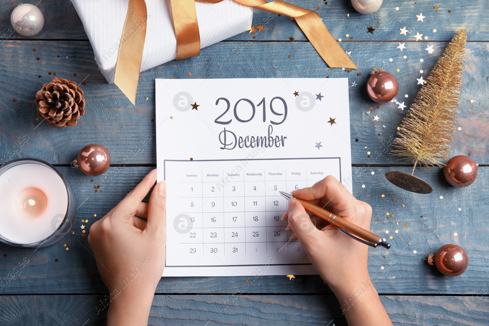 Photo of Woman marking date in calendar at blue wooden table, top view