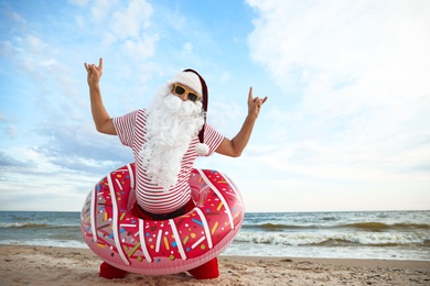 Photo of Santa Claus with inflatable ring having fun on beach, space for text. Christmas vacation