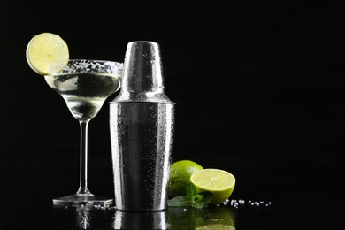 Metal shaker, delicious cocktail, limes and mint on black mirror surface, space for text