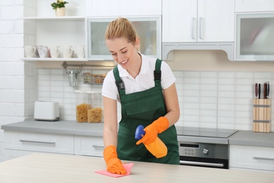 Female janitor cleaning table with rag in kitchen