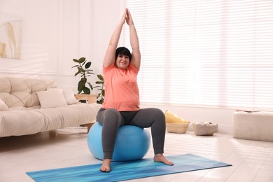 Overweight mature woman doing exercise with fitness ball at home
