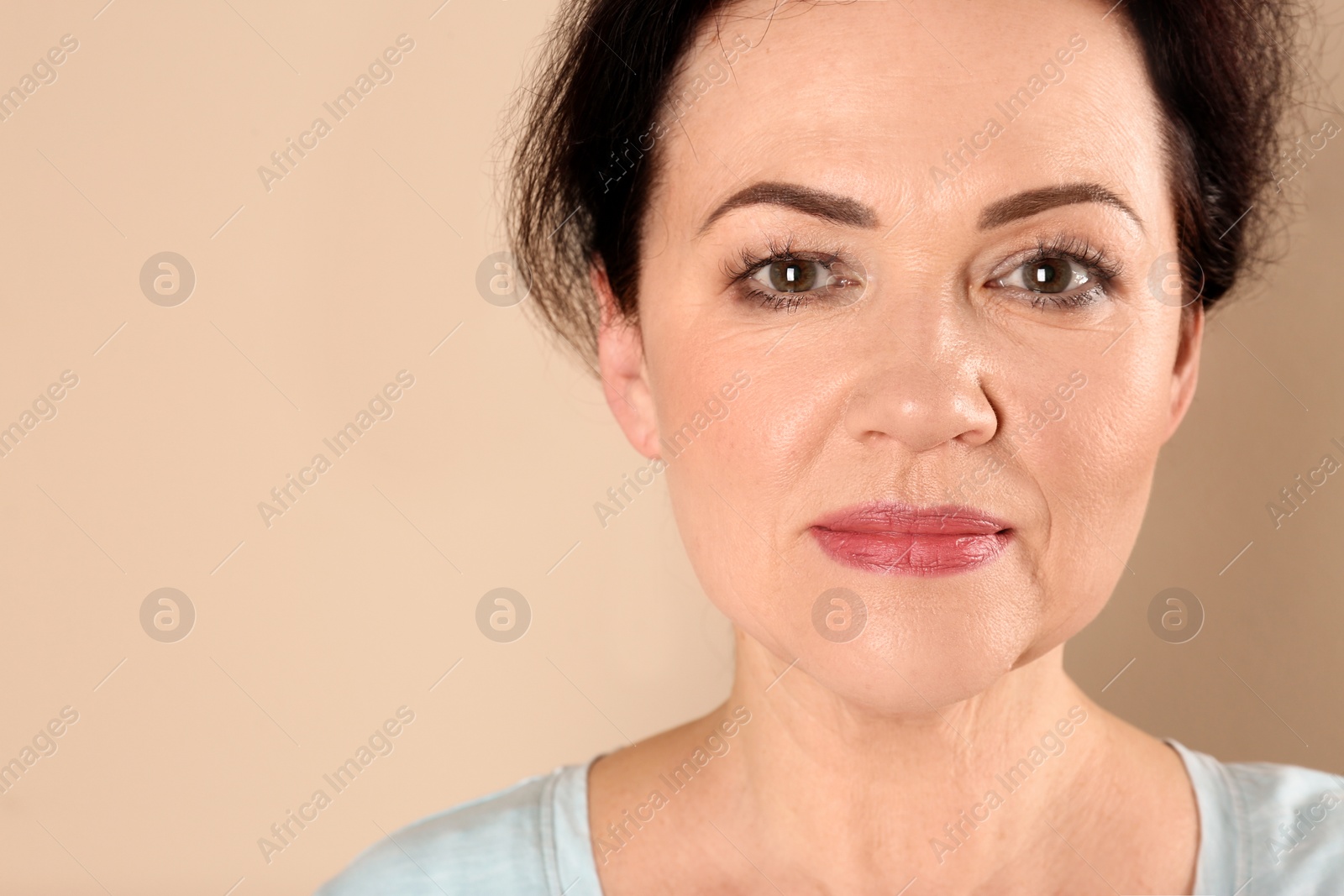 Photo of Portrait of charming mature woman with healthy beautiful face skin and natural makeup on beige background, closeup. Space for text