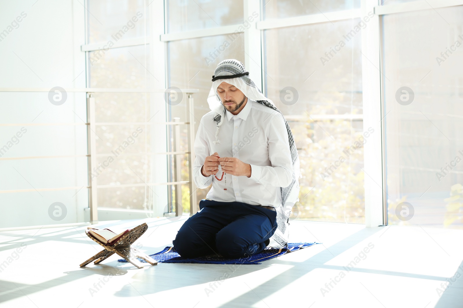 Photo of Muslim man with Koran praying on rug indoors