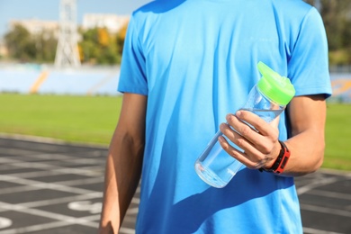 Photo of Sporty man holding bottle of water at stadium on sunny day, closeup