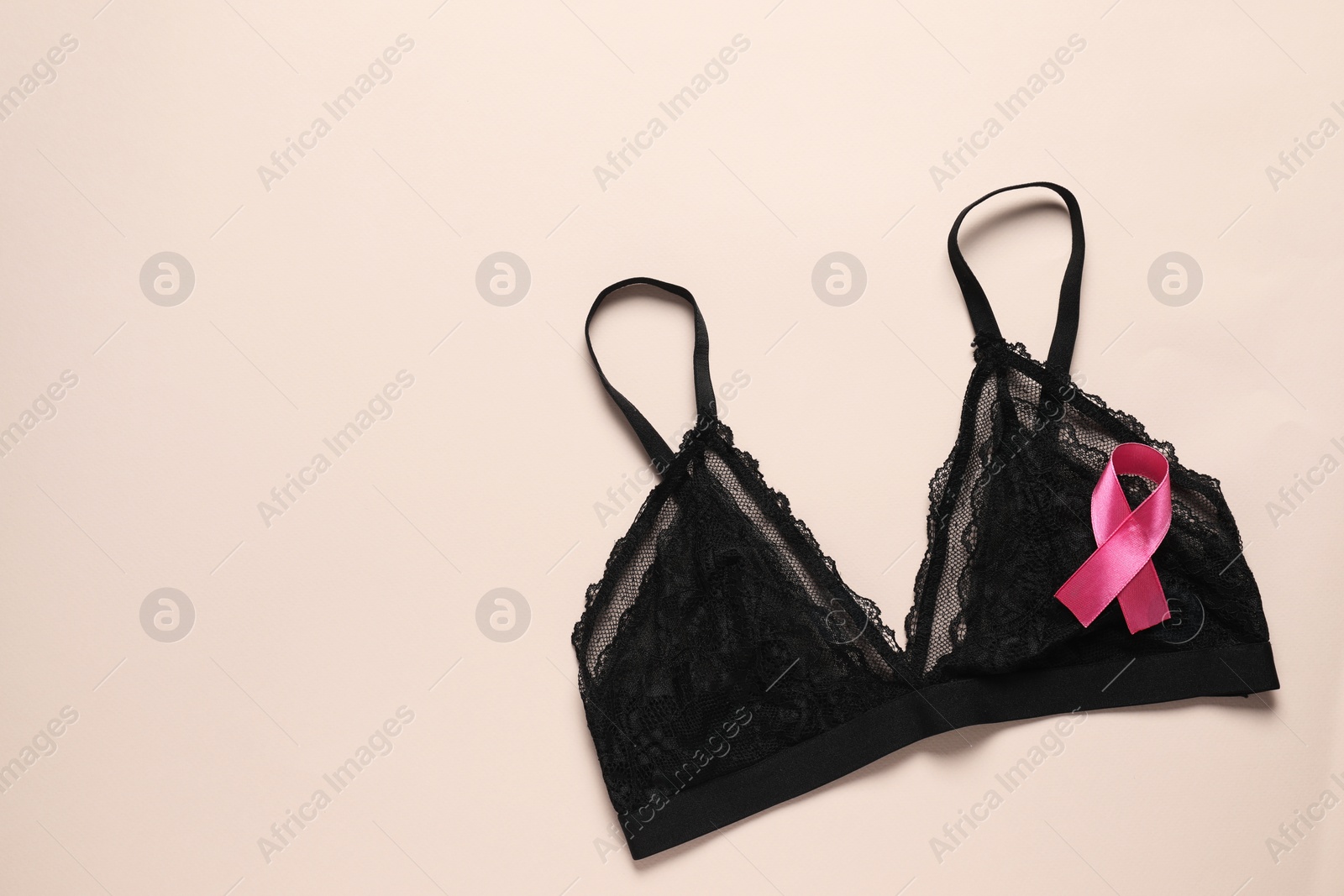 Photo of Pink ribbon and bra on beige background, top view with space for text. Breast cancer awareness