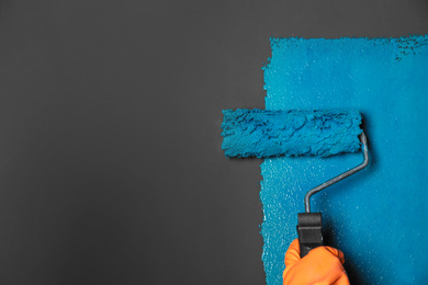 Photo of Woman painting grey wall with blue dye, closeup. Space for text