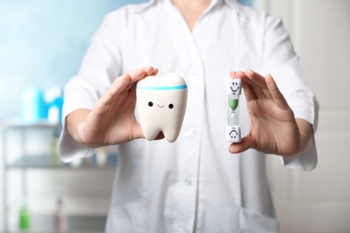 Photo of Dentist holding model of tooth and sand glass at workplace, closeup view