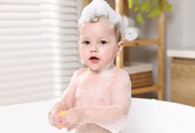 Photo of Cute little child playing with toy duck in bathtub at home