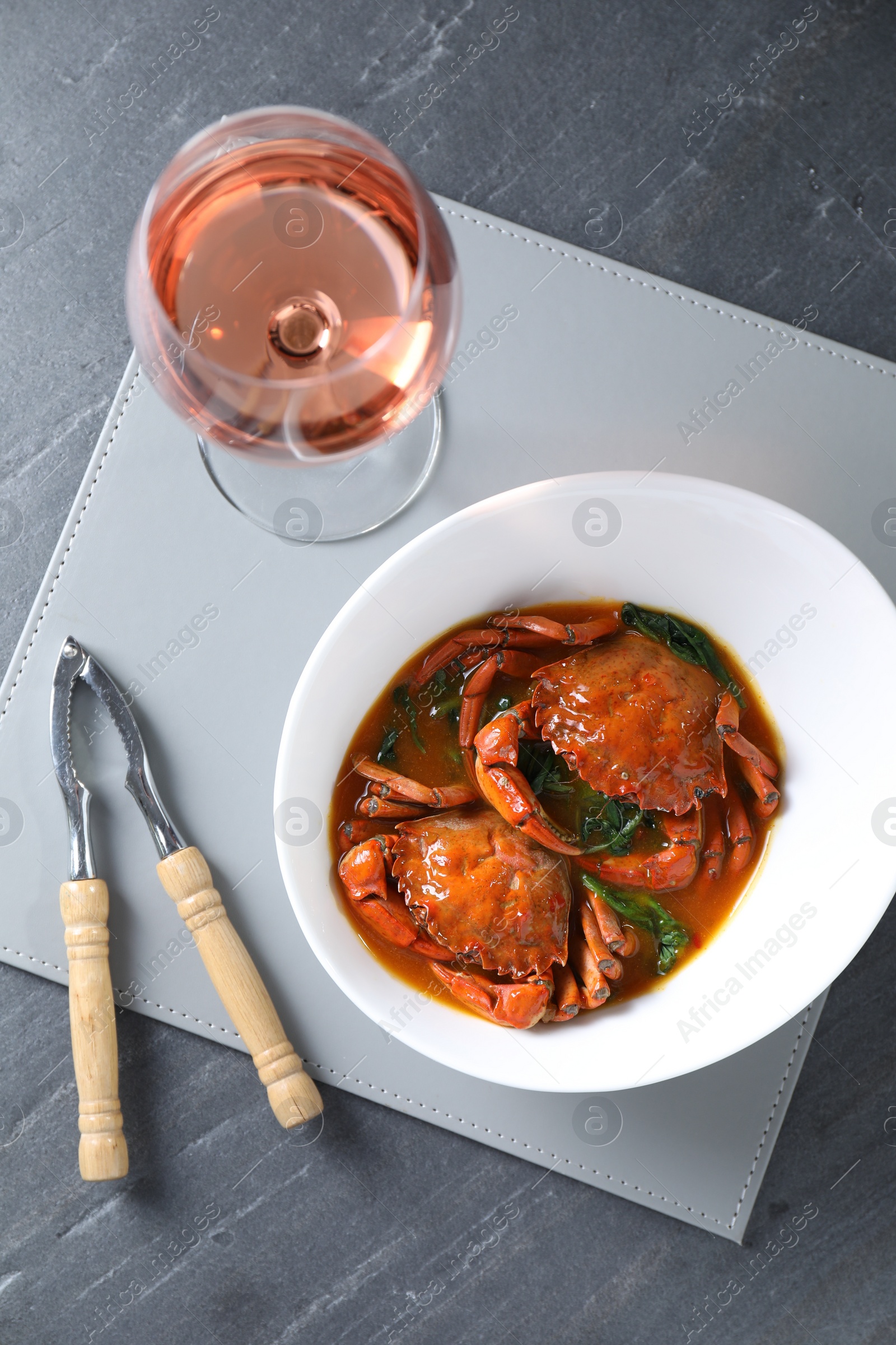 Photo of Delicious boiled crabs with sauce, glass of wine and cracker on grey table, top view