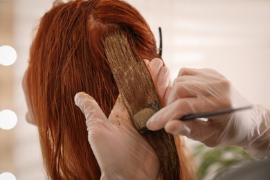 Photo of Professional hairdresser dyeing woman's hair with henna on blurred background, closeup