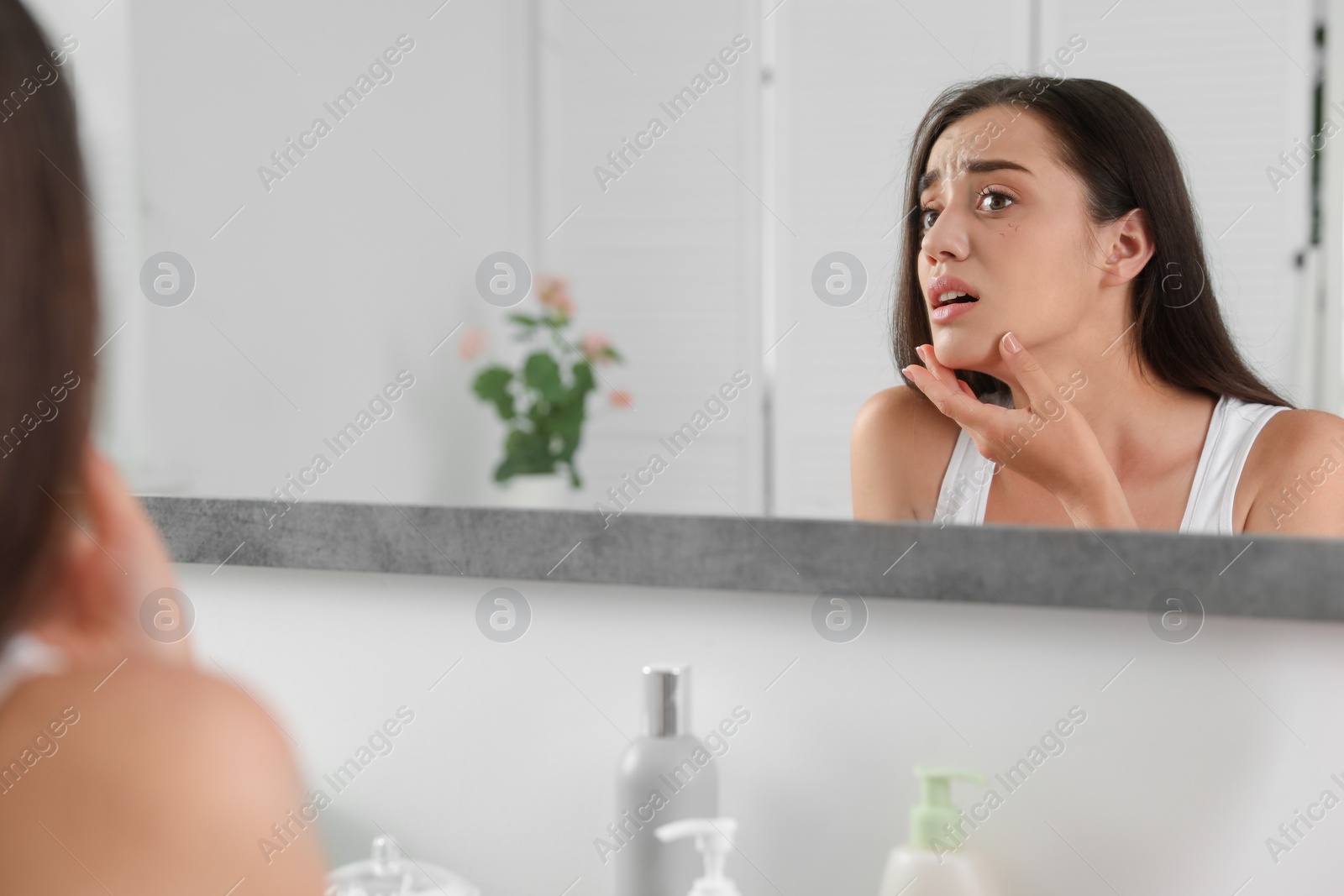 Photo of Young woman with eyelash loss problem looking in mirror indoors