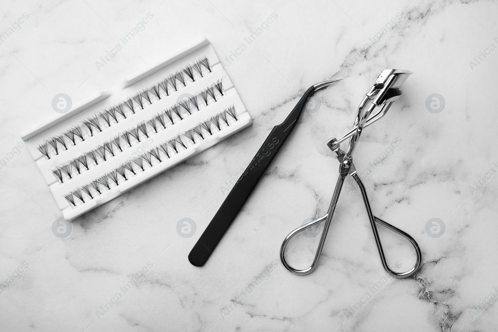 Photo of Artificial eyelashes and accessories on marble background, flat lay