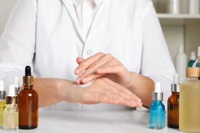 Photo of Dermatologist testing cosmetic product at white table indoors, closeup