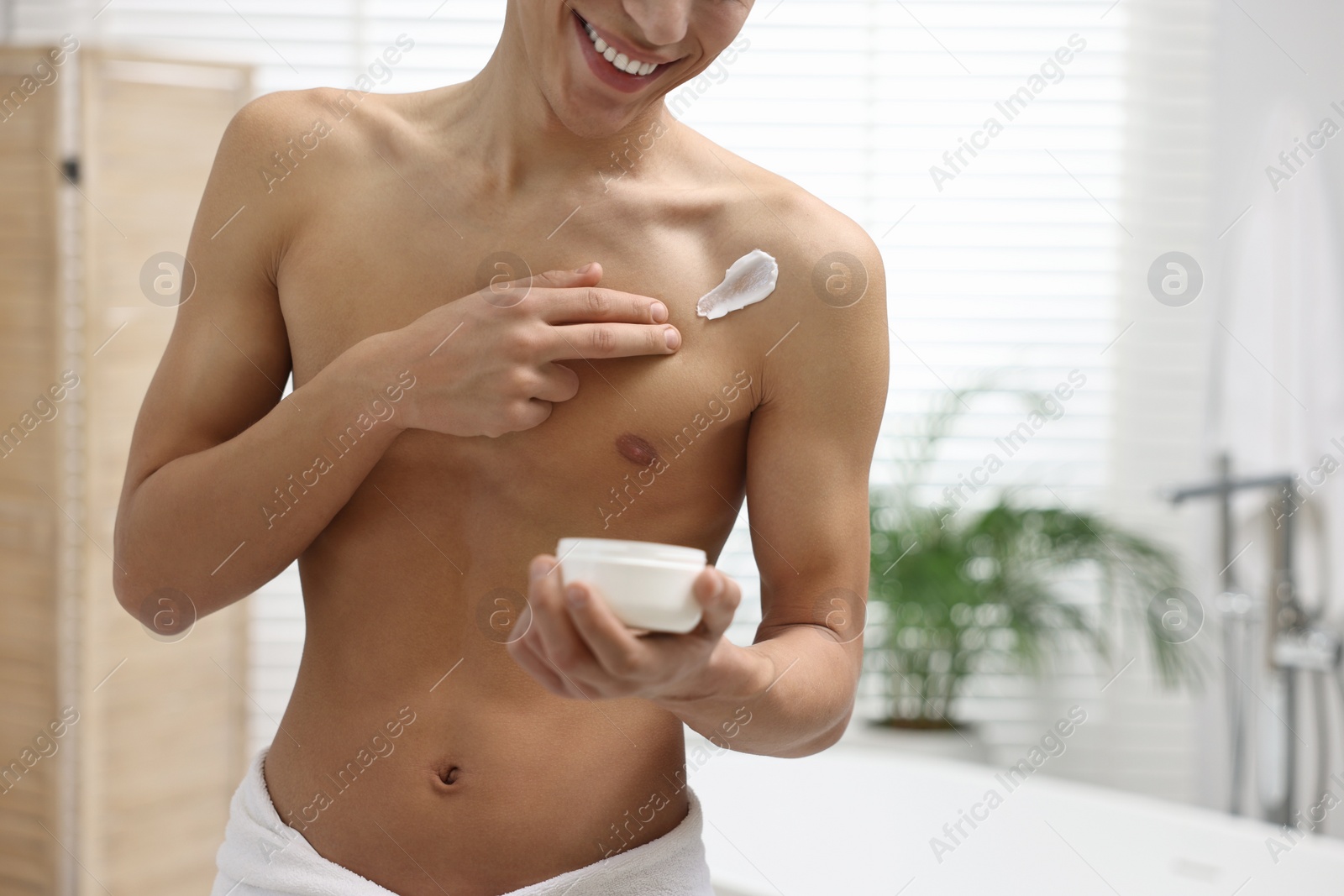 Photo of Man applying moisturizing cream onto his shoulder in bathroom, closeup. Space for text