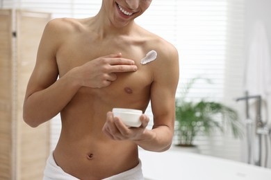 Man applying moisturizing cream onto his shoulder in bathroom, closeup. Space for text