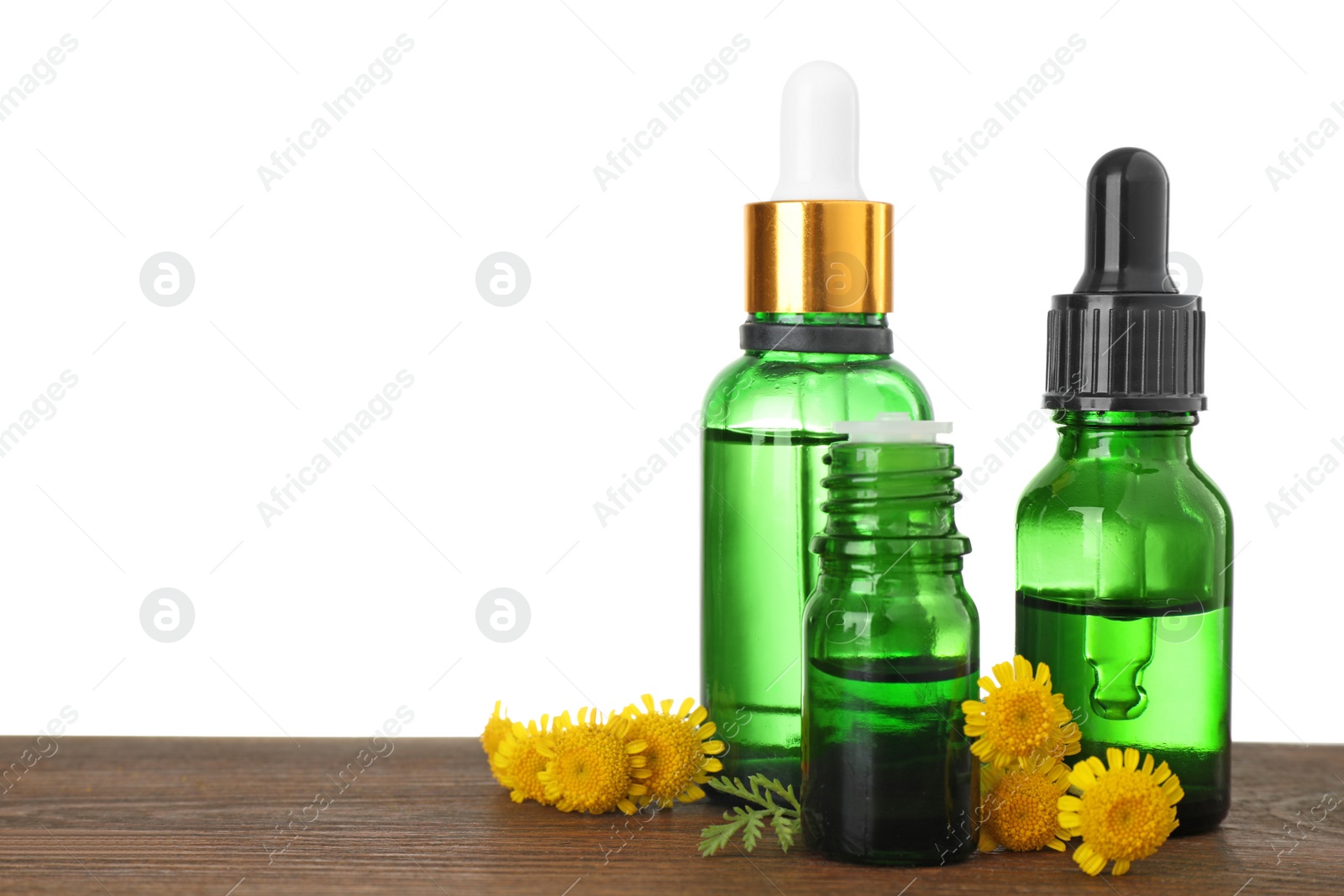 Photo of Bottles of herbal essential oils, pipette and flowers on wooden table, white background