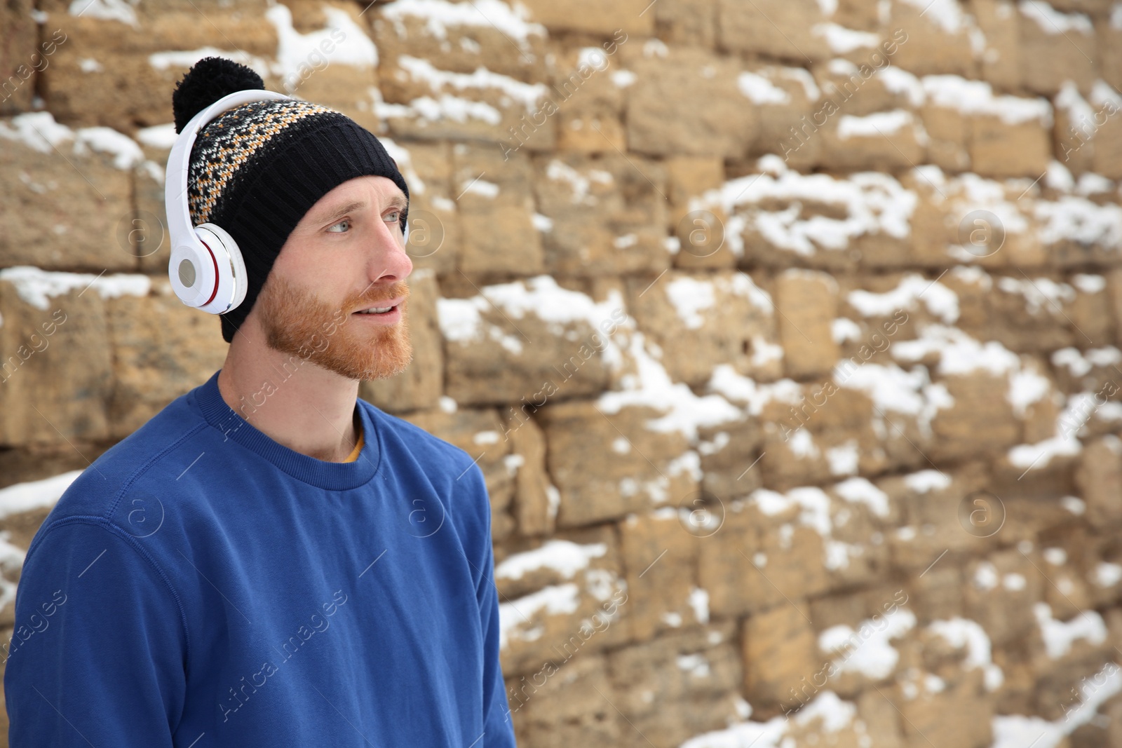 Photo of Young man listening to music with headphones against stone wall. Space for text