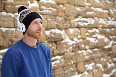 Young man listening to music with headphones against stone wall. Space for text